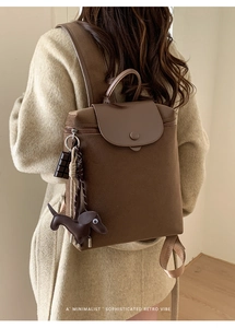Detail of dark brown canvas backpack featuring leather flap and cute dachshund charm