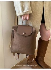 Close-up of brown vintage backpack with leather flap and buckle on a beige coat outfit