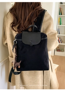 Detail of black velvet backpack with leather flap and brown horse charm against beige coat