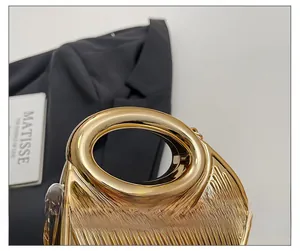 Détail du sac de soirée doré avec plis verticaux et poignée métallique ronde