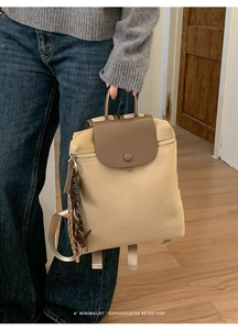 Detail of retro beige canvas backpack with brown leather trim and woven charm accessory