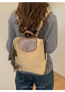 Rear view of a khaki canvas backpack with brown leather flap and a cute dog charm pendant