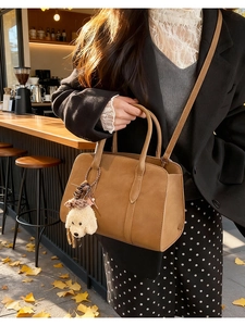 Close-up of brown suede crossbody bag with poodle charm in an autumn street scene