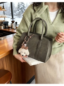 Olive green suede crossbody bag with leopard print poodle charm shown in a winter cafe scene