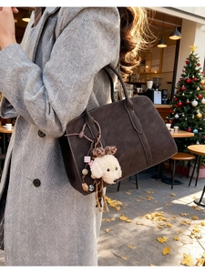 Detail of dark brown suede shoulder bag with a cute white puppy plush charm on the strap