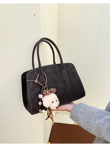 Detail of dark brown suede handbag featuring cute plush puppy and leopard bow charms