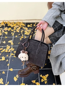 Detail view of a vintage dark brown suede crossbody bag with a cute puppy plush charm