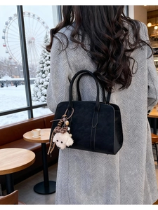Detail of black suede shoulder bag featuring a cute plush dog pendant charm in a cafe