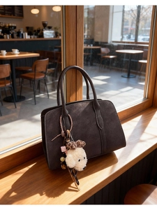 Detail of vintage suede shoulder bag with cute white plush dog pendant in sunlight