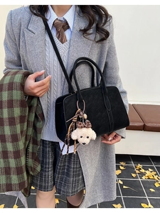 Detail of black suede crossbody bag with a cute plush puppy charm and leopard bow