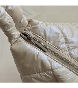 Macro detail of silver metal zipper on beige quilted padded handbag with satin finish