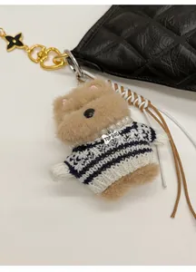 Detail of plush puppy bag charm with striped sweater and bone tag on black quilted purse
