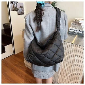Detail of a large black quilted puffer shoulder bag with a soft padded strap for comfort