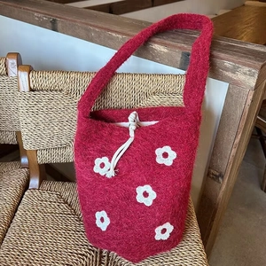 Detail of red knit bucket bag with white floral embroidery and cotton drawstring closure