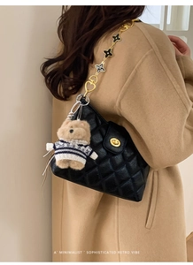 Detail of black quilted leather bag with gold chain and plush bear charm on beige coat