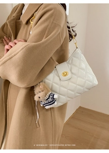 Detail of white quilted crossbody bag with gold rotary lock and cute dog pendant