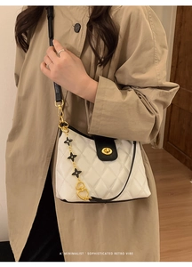 Detail of white quilted crossbody bag with black leather flap and floral chain charm