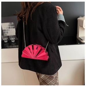 Detail of fan-shaped fuchsia evening bag with gold chain worn with a chic black suit
