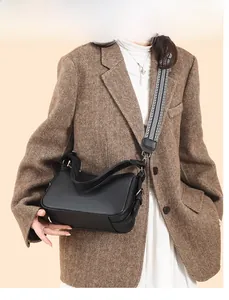 Detail of black pebbled leather crossbody bag with geometric striped wide strap on model