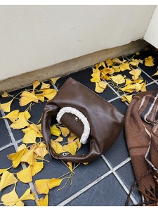 Détail du sac à main marron foncé avec bordure en fourrure sur feuilles d'automne