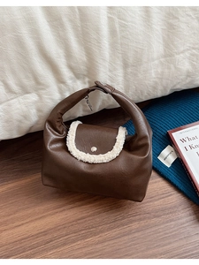 Détail du sac à main en cuir marron avec bordure en laine mouton crème et bouton métal