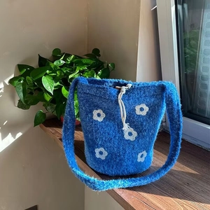 Blue and white knit floral shoulder bag with drawstring closure on a sunny windowsill