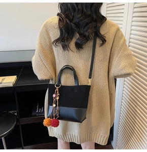 Detail of black contrast stitch bucket bag with colorful pompom charm on beige knit sweater