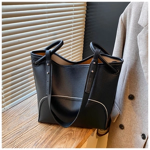 Close-up of black lychee grain leather tote bag on wooden surface with natural lighting