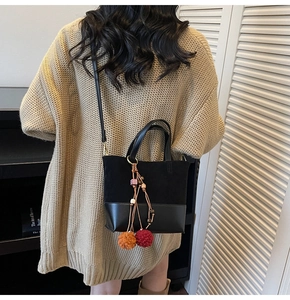 Detail of a black patchwork handbag with suede texture, shoulder strap and colorful pompom