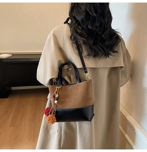 Detail view of two-tone contrast tote bag featuring suede finish and colorful tassel charm