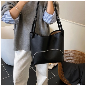 Detail of black pebbled leather tote bag with white wavy piping and adjustable straps