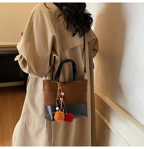 Detail of color-block tote bag with suede texture and decorative tassel on a beige coat