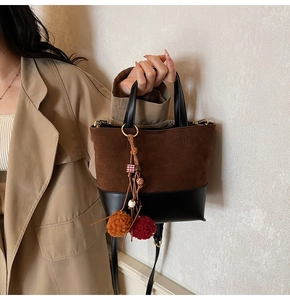 Detail of color-block bucket bag with brown suede and black leather, pompom and tassel decor