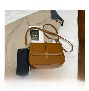 Detailed view of brown leather crossbody bag with metal buckle next to a smartphone