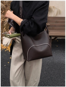 Detail of dark brown leather bucket bag featuring white contrast stitching and soft texture