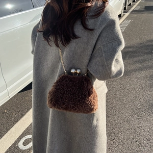 Detailed view of dark brown plush chain bag with golden kiss-lock on a grey coat