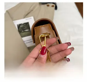 Detailed close-up of gold metal hook and brown leather strap on minimalist shoulder bag