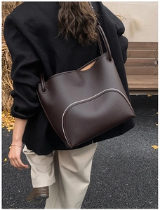 Outdoor shot of a dark brown leather tote bag with white trim and pebbled texture