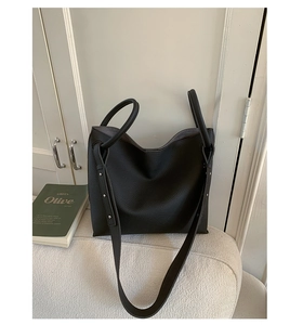 Macro shot of black pebbled leather tote bag with metallic side studs on a white sofa