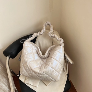 Chic beige quilted puffer tote bag with scrunchie handle on a black leather chair