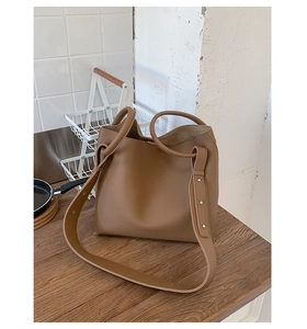 Detail of dark camel pebbled leather bucket bag with metal ring handles and wide strap