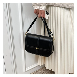 Detail of minimalist black crossbody bag with gold buckle on a white dress backdrop