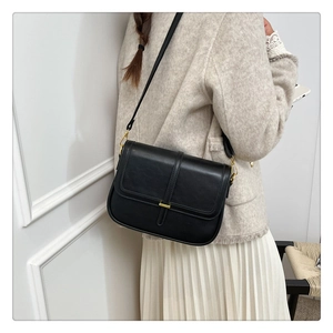 Detail of black leather crossbody bag with gold metal buckle and thin shoulder strap