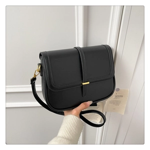 Detail of a black leather saddle bag featuring a minimalist gold metallic lock and flap