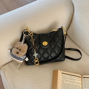 Chic black quilted crossbody bag with golden hardware and plush dog charm on a sofa