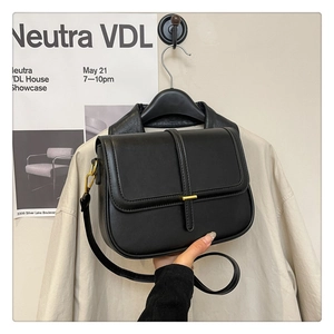Detail of black faux leather crossbody bag with gold metallic buckle and textured finish