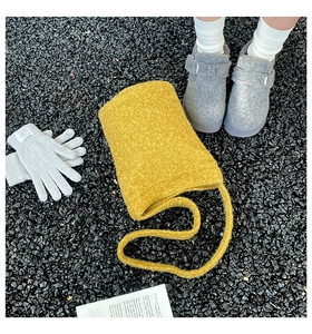 Outdoor flat lay of a mustard yellow felt bucket bag, grey knit gloves and plush ankle boots