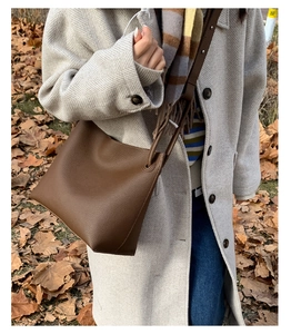 Close-up of brown pebbled leather bucket bag with shoulder strap on a winter wool coat