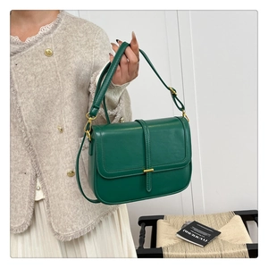 Detail of dark green square crossbody bag featuring a golden metal clasp on gray coat
