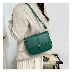 Detail of dark green flap crossbody bag with gold metal hardware and adjustable strap